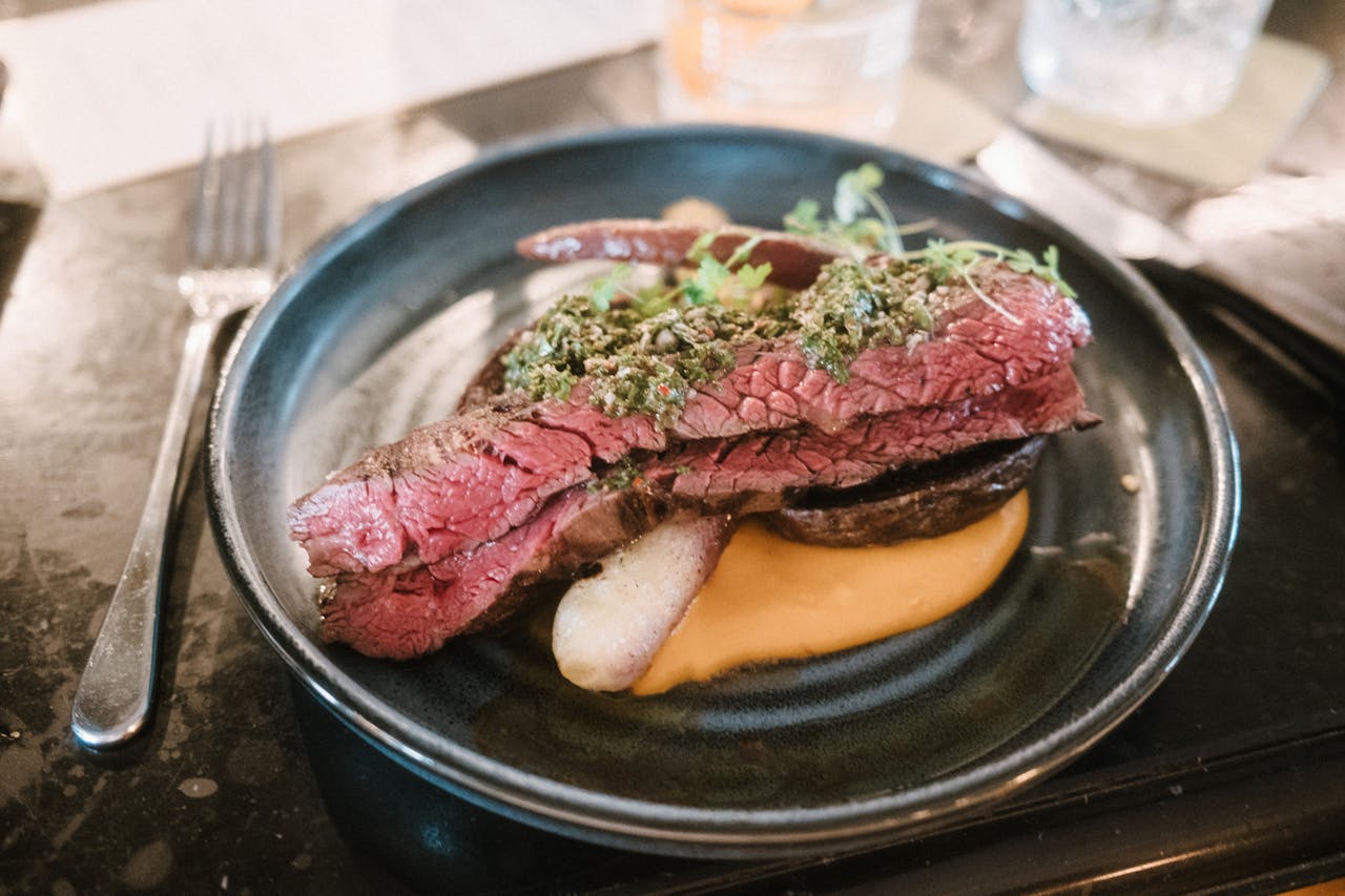Deliciously plated steak with chimichurri sauce on a black plate, perfect for gourmet dining enthusiasts.
