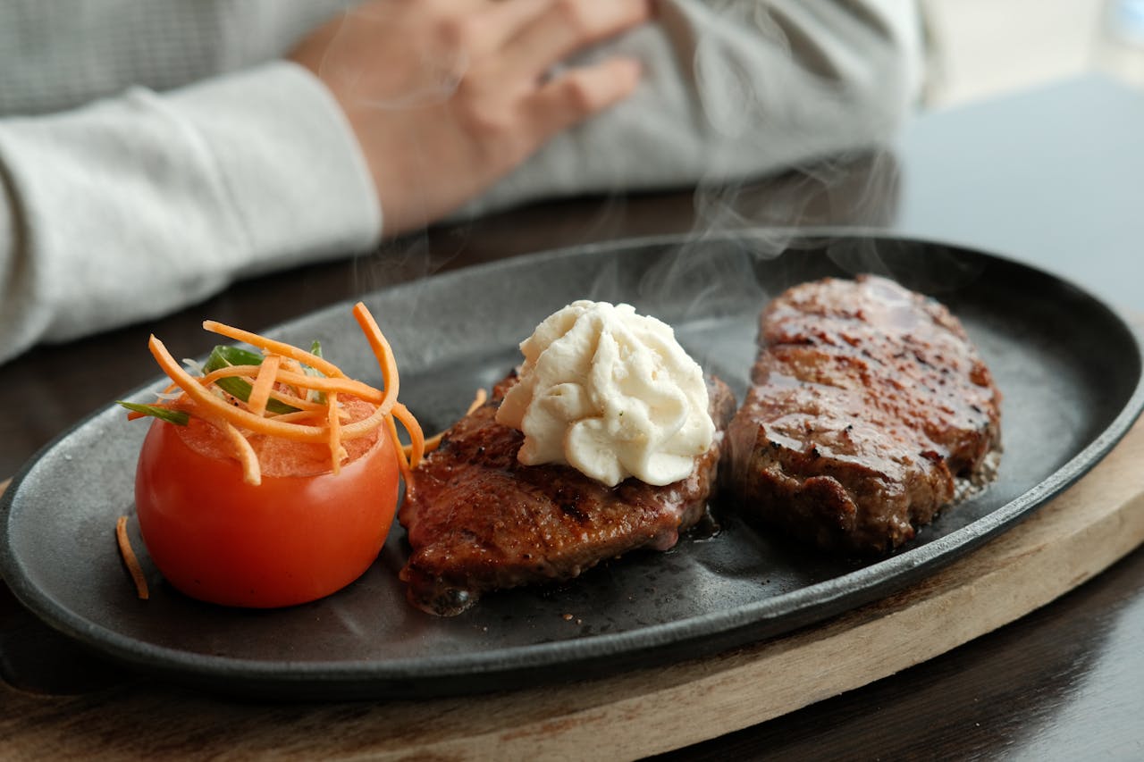 A sizzling steak served with tomato and whipped butter, perfect for food photography.