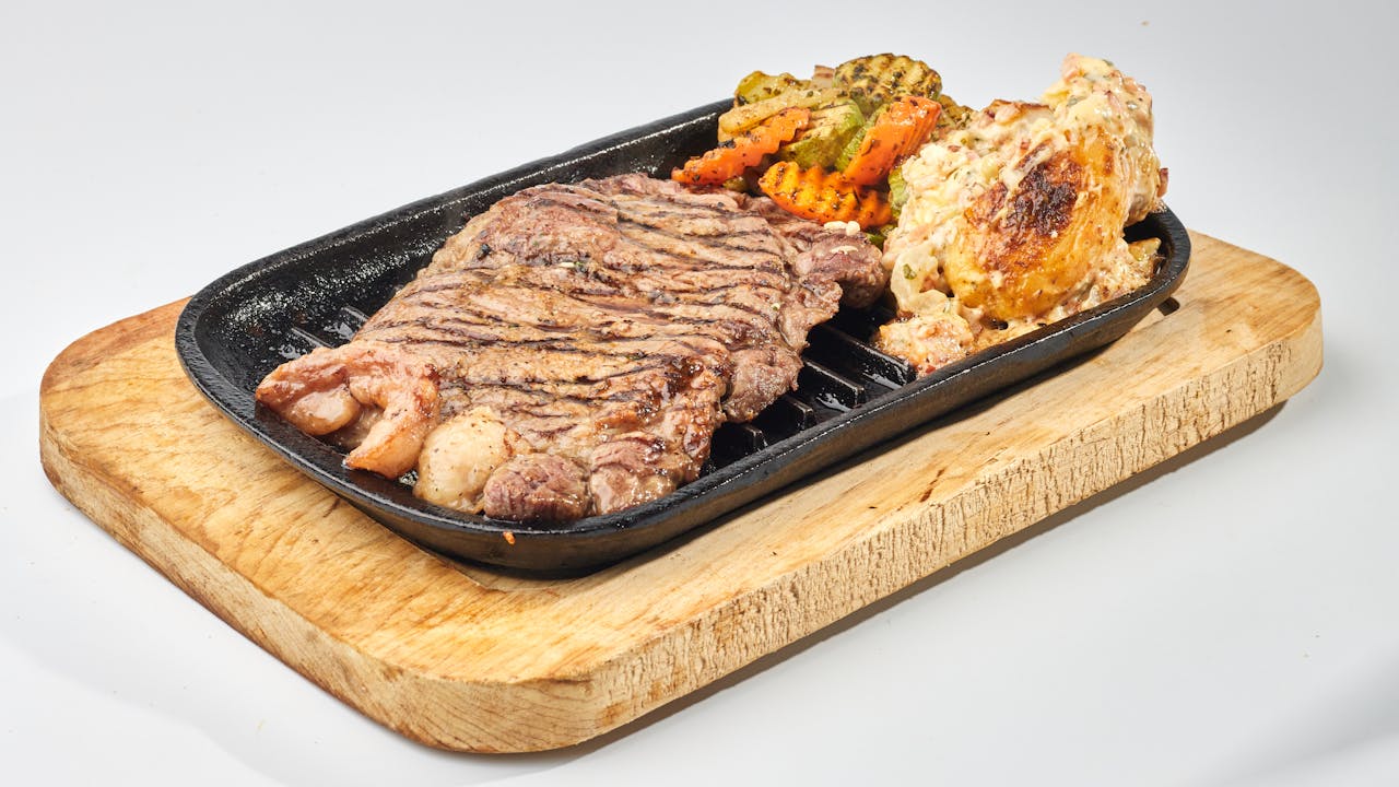 Sizzling grilled steak served with colorful roasted vegetables on a wooden board.