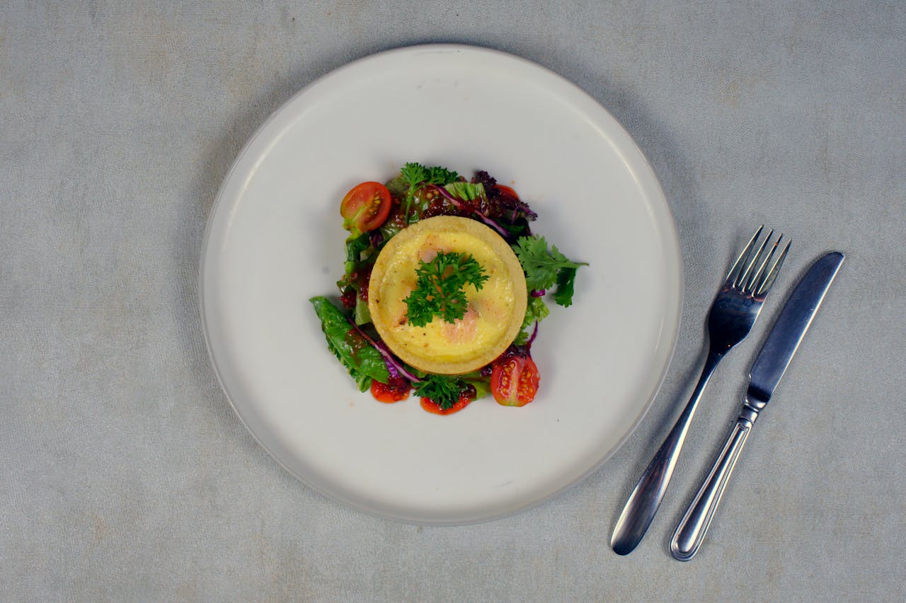 Top view of a vibrant salad with quiche and cherry tomatoes on a white plate.