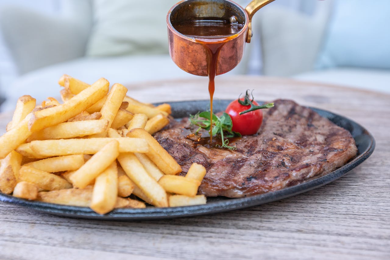A delectable steak served with french fries, drizzled with sauce, on a wooden table.