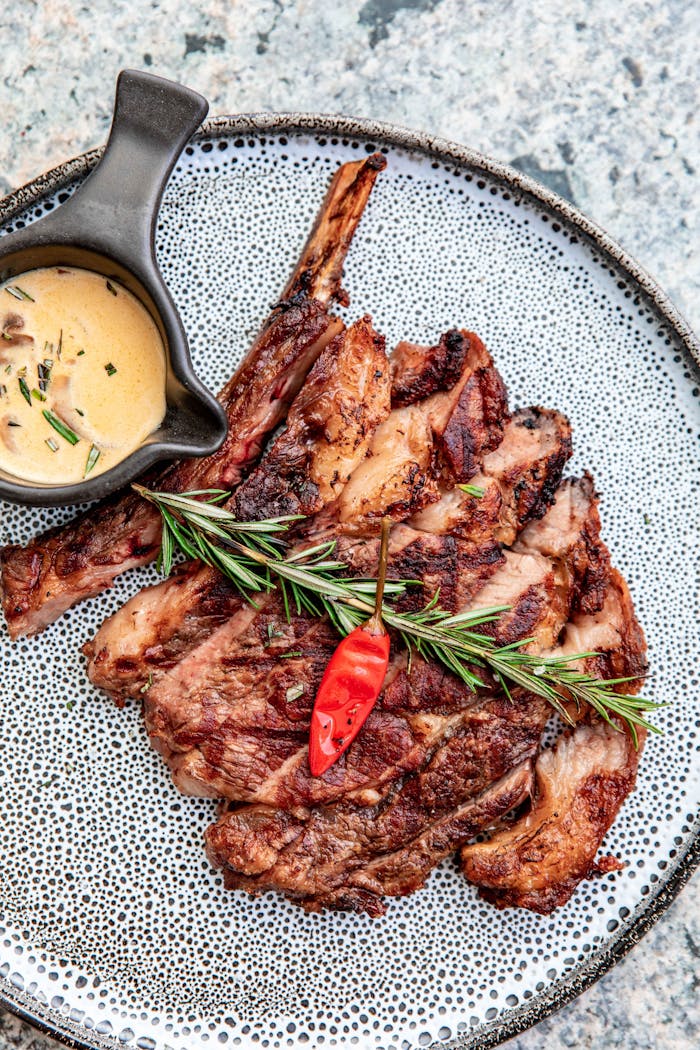 Juicy ribeye steak garnished with rosemary and chili pepper, served with creamy sauce.